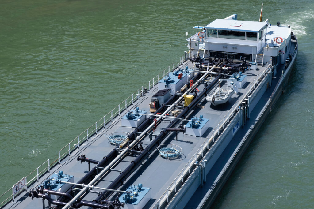 BASEL, SWITZERLAND - JULY 10 2022: Barge seen from above with pipelines on the deck for industrial transport of oil and gas on the river Rhine in Basel. Seen from above. Energy transport